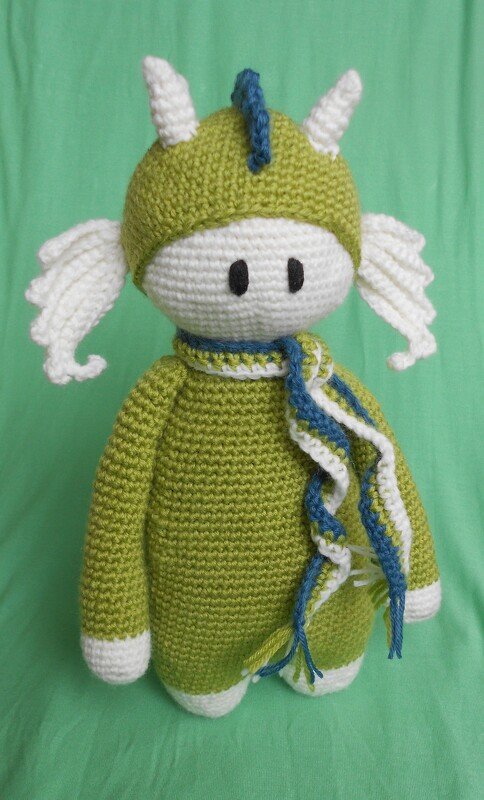 Gehäkelter Amigurumi-Drache in Grün und Weiß mit blau-grün gestreiftem Schal, Hörnern und Flügelchen.