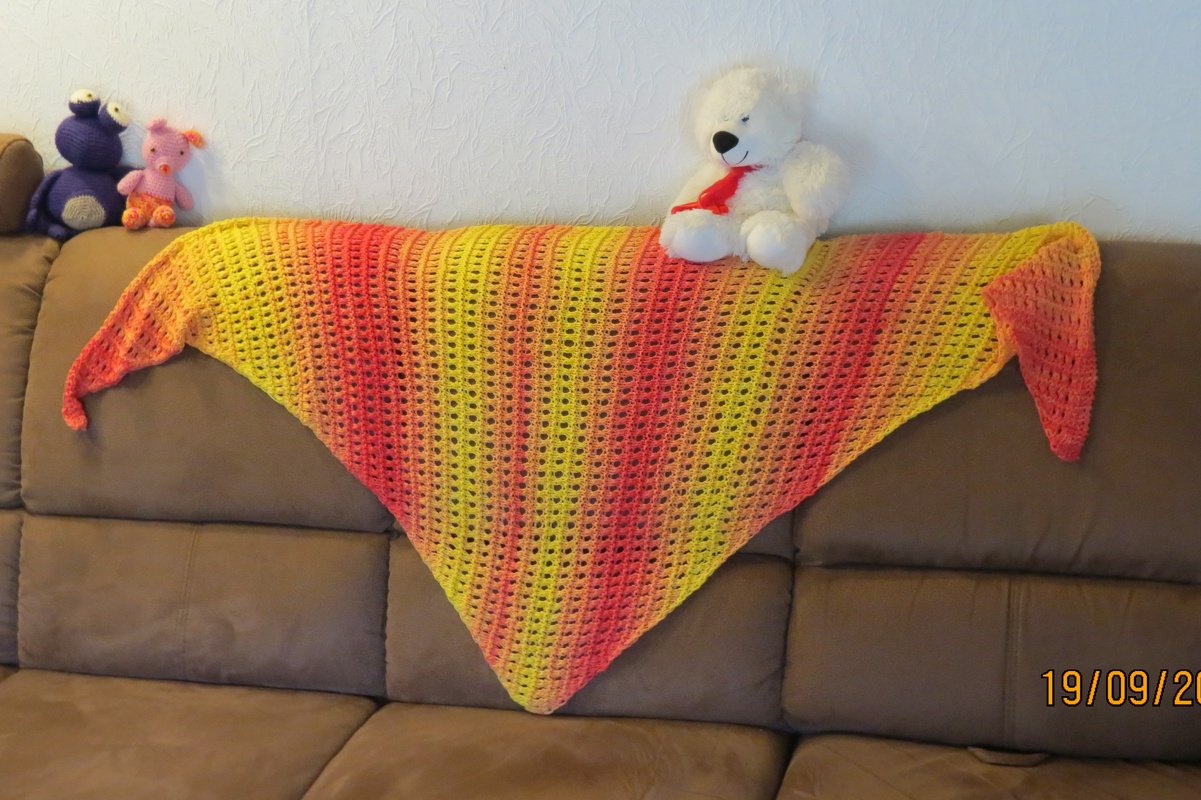 Gestricktes Dreieckstuch in Gelb- und Orangetönen mit Lochmuster auf braunem Sofa
