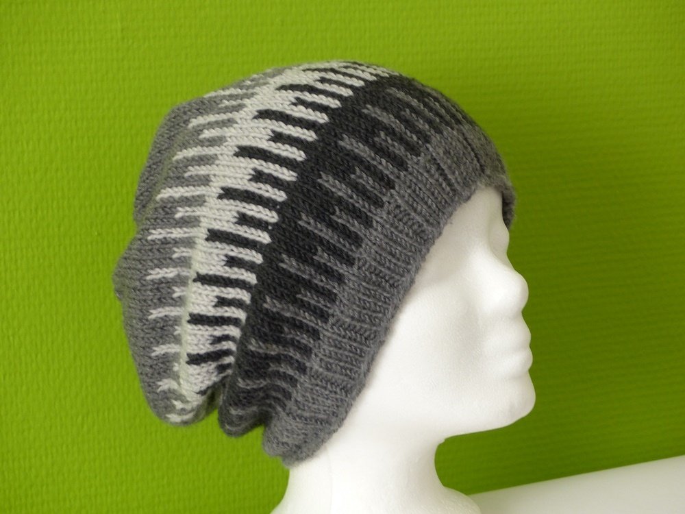 Detailansicht einer gestrickten Slouch-Mütze mit Rippenbund und Streifen in Grautönen und Weiß