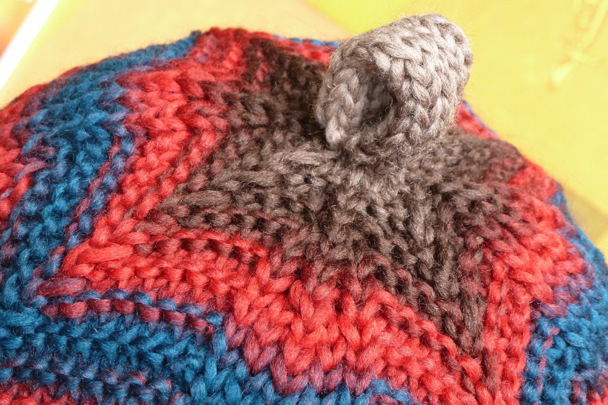 Nahaufnahme einer grob gestrickten Kinder-Mütze mit blau-roten und grauen Streifen und spitz zulaufendem Oberteil