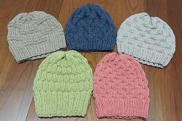 Fünf gestrickte Beanies in Sand, Dunkelblau, Hellgrau, Lindgrün und Koralle auf Holzuntergrund, mit Rippenbündchen und strukturiertem Strickmuster