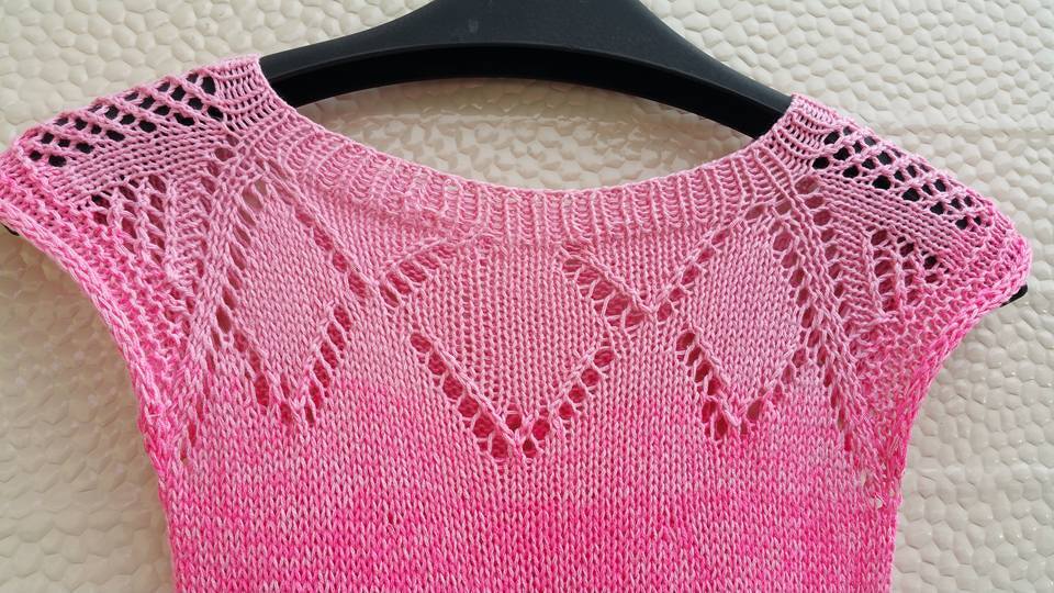 Detailaufnahme eines rosa gestrickten Kinder-Oberteils mit Lochmuster an der Rundpasse und Farbverlauf, auf einem Bügel.