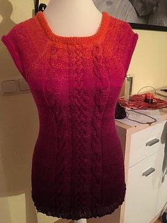 Gestrickte ärmellose Tunika auf Schneiderbüste mit zentralem Zopfmuster und orange‑bis‑magenta Farbverlauf
