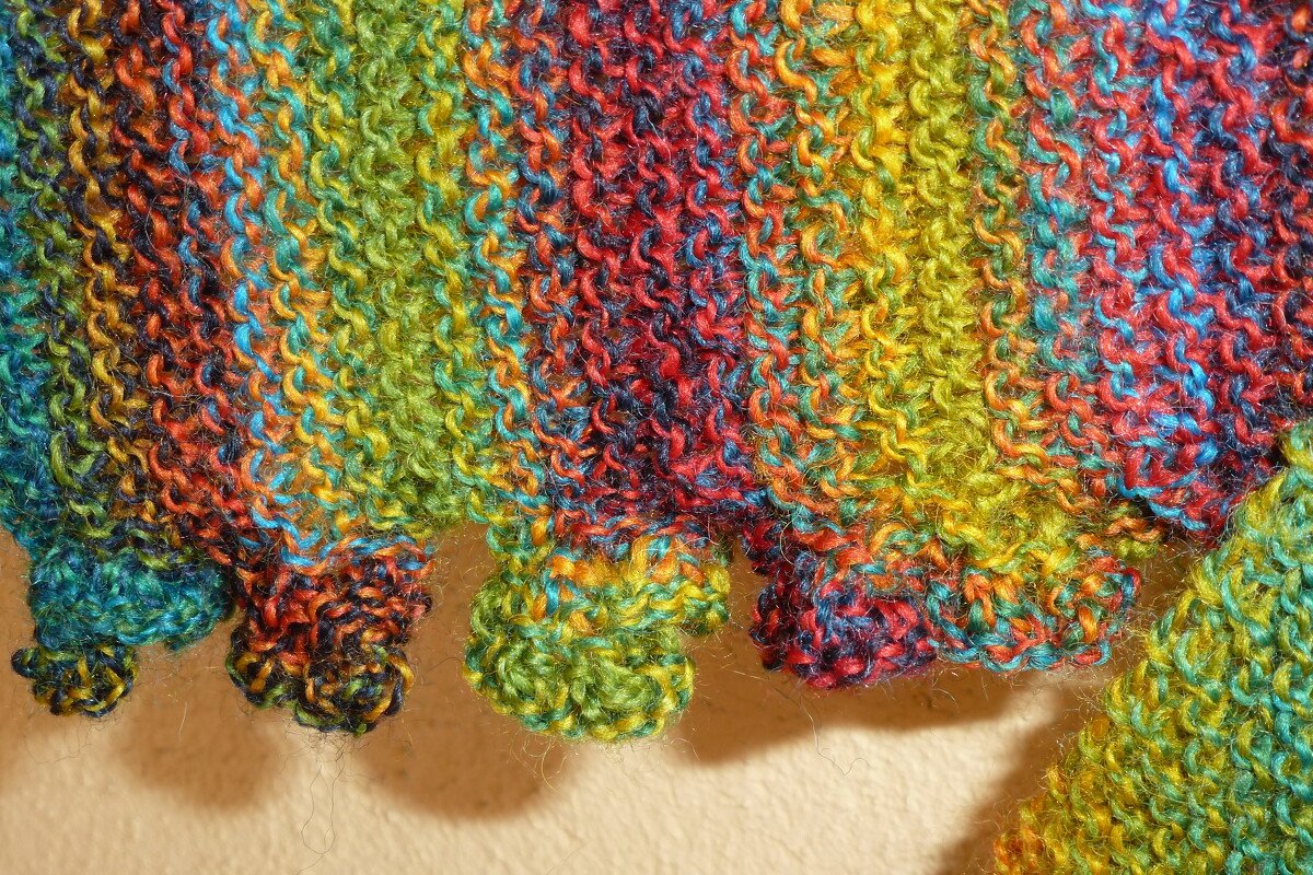 Nahaufnahme eines bunten, kraus-rechts gestrickten Stoffs mit regenbogenfarbener Musterung und gewelltem Saum