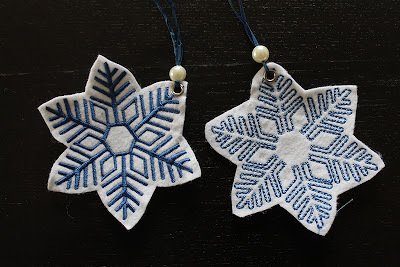 Nahaufnahme zweier weißer Filz-Schneeflocken mit unterschiedlichen blauen Stickmustern und Aufhängungen