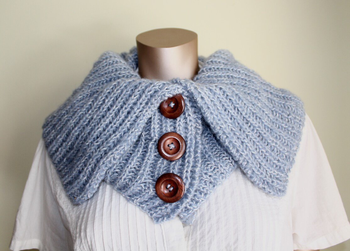 Hellblauer, gerippter Kragenschal mit drei braunen Holzknöpfen auf Schaufensterpuppe über weißer Bluse
