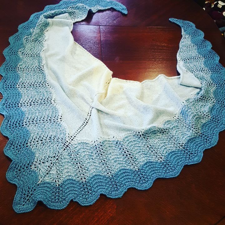 Gestricktes zweifarbiges Dreieckstuch in Weiß und Blau mit welligem Ajourrand auf dunklem Tisch