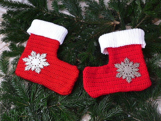 Zwei rote gehäkelte Weihnachtsstrümpfe mit weißen Bündchen und Schneeflocken auf Tannenzweigen