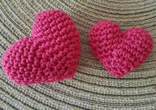 Zwei gehäkelte Herzen in Rosa und Rot nebeneinander auf einem strukturierten Stoff