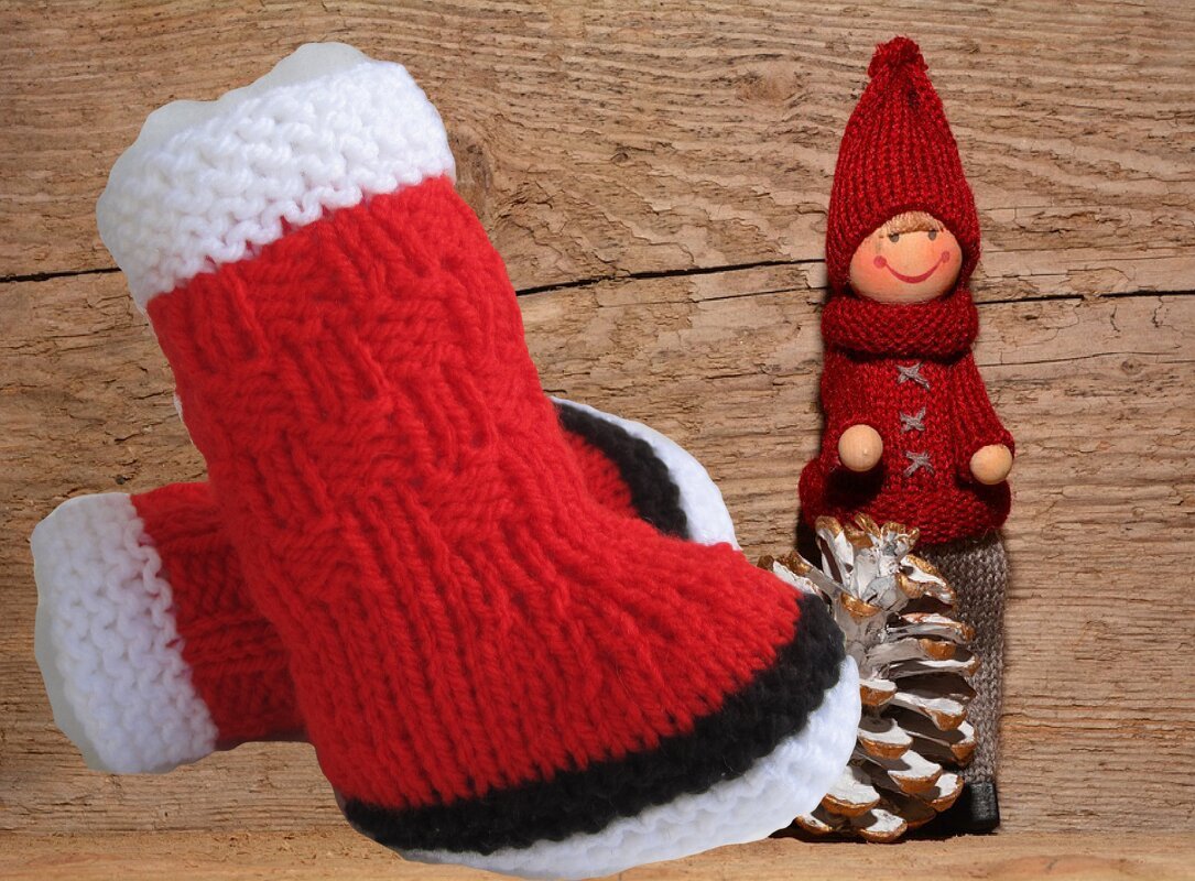 Weihnachtliche rote Babyschuhe neben Holz-Wichtel und Tannenzapfen auf Holzbrett