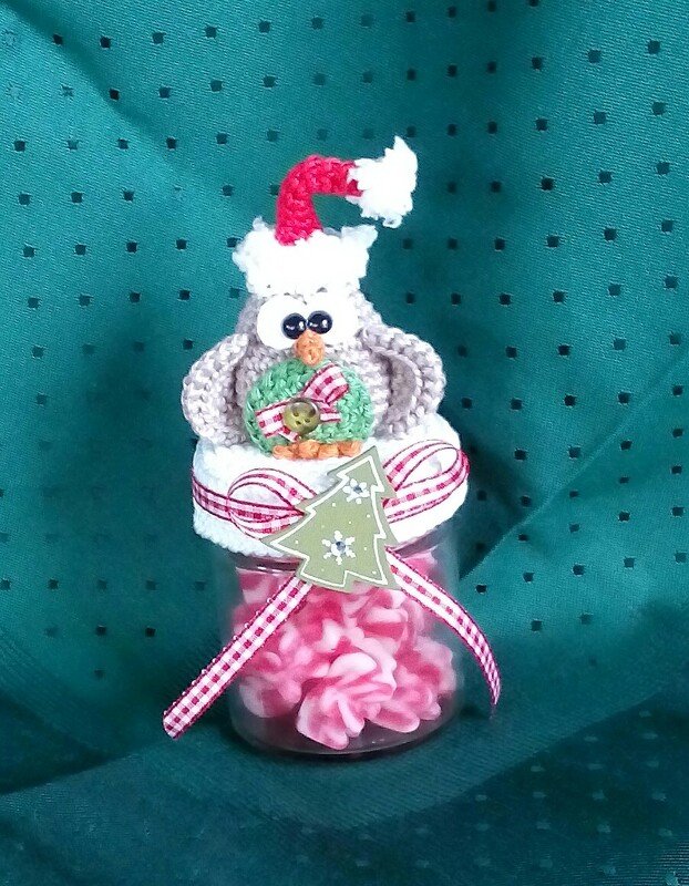 Gehäkelte Weihnachtseule mit roter Mütze und Kranz auf einem festlich verzierten Glas voller Süßigkeiten