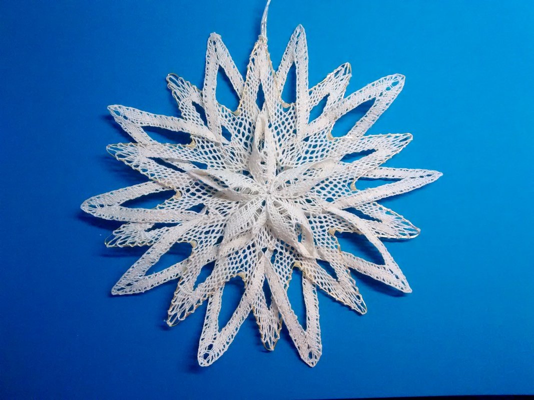 Zarter weißer Spitzenstern mit mehrlagigem Lochmuster vor blauem Hintergrund