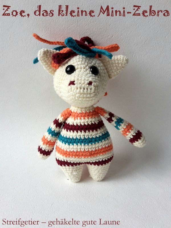 Gehäkeltes Amigurumi-Mini-Zebra mit bunten Streifen (Orange, Dunkelrot, Türkis), schwarzen Knopfaugen und farbiger Mähne.