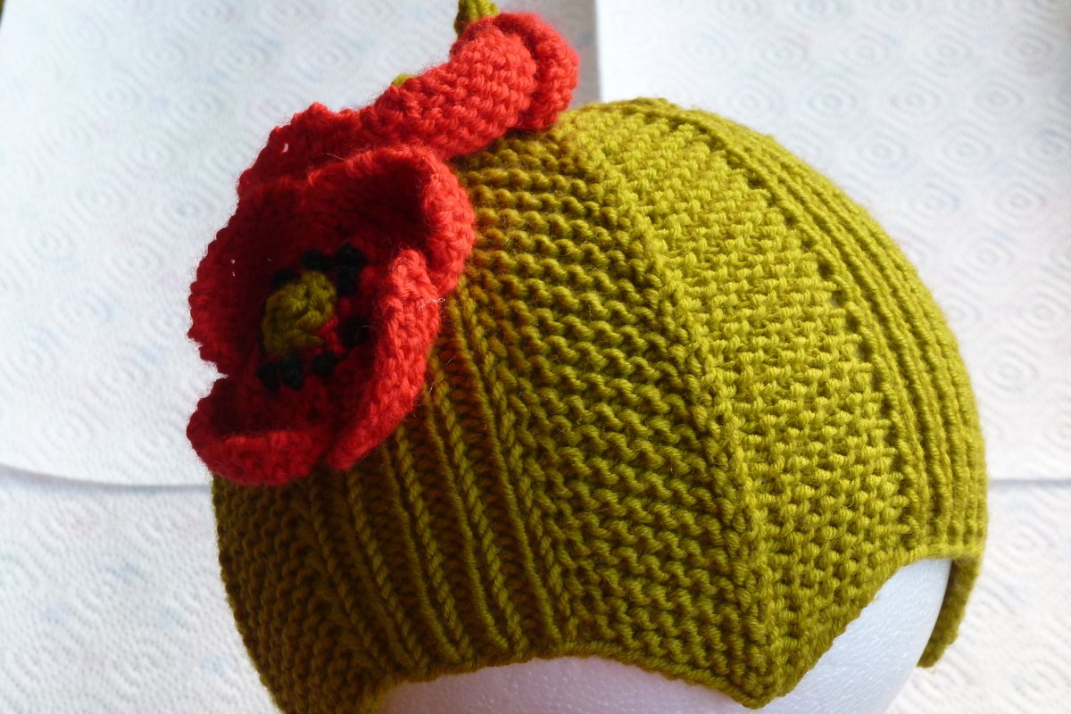 Gestrickte olivgrüne Kindermütze mit roter Mohnblume auf weißem Hintergrund
