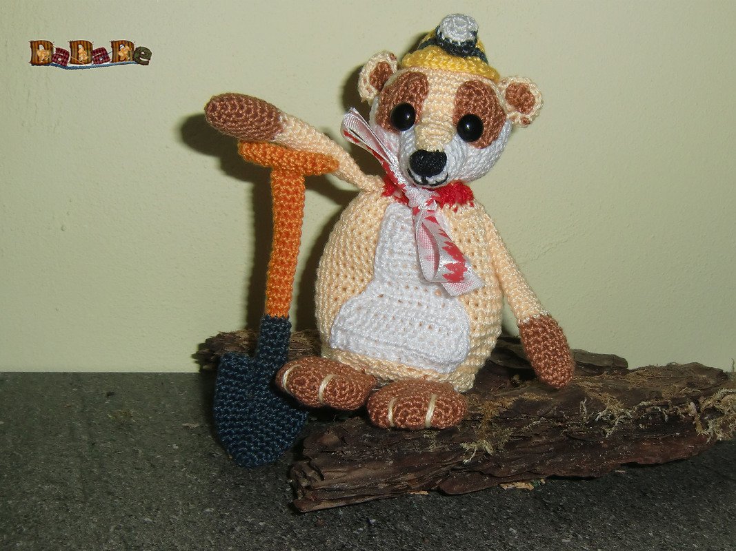 Gehäkeltes Amigurumi-Tier sitzend mit Schleife, Häubchen und gehäkelter Schaufel