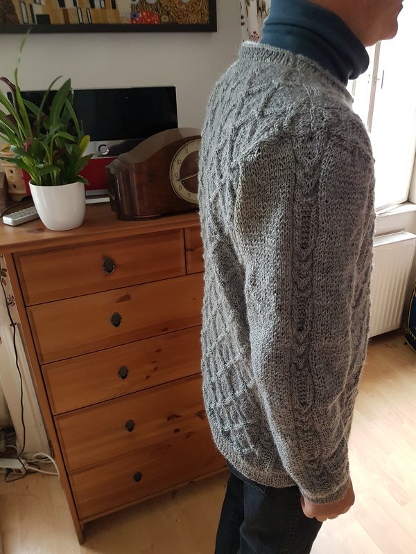 Seitenansicht einer Person in grauem gestrickten Herrenpullover mit Zopfmuster