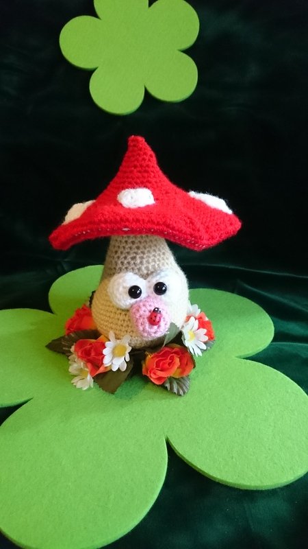 Gehäkelter Fliegenpilz-Amigurumi mit rotem Punkt-Hut und Blumenkranz auf grünen Filz-Kleeblättern