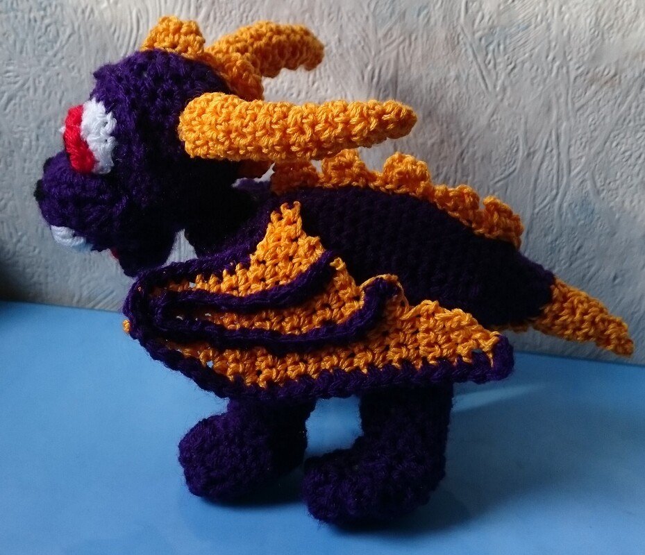 Nahaufnahme eines gehäkelten lila-gelben Amigurumi-Drachens mit Fokus auf Flügel- und Horndetails