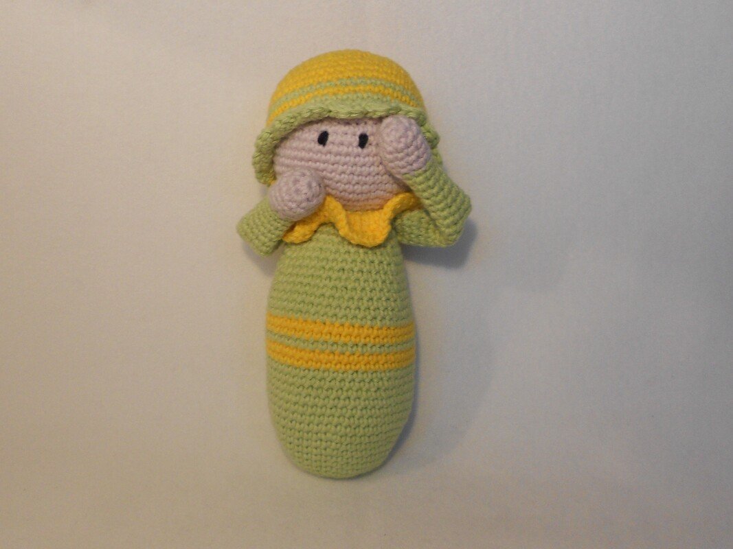 Amigurumi-Puppe mit ovalem Körper, angesetzten Armen, Mütze und gelbem Rüschenkragen