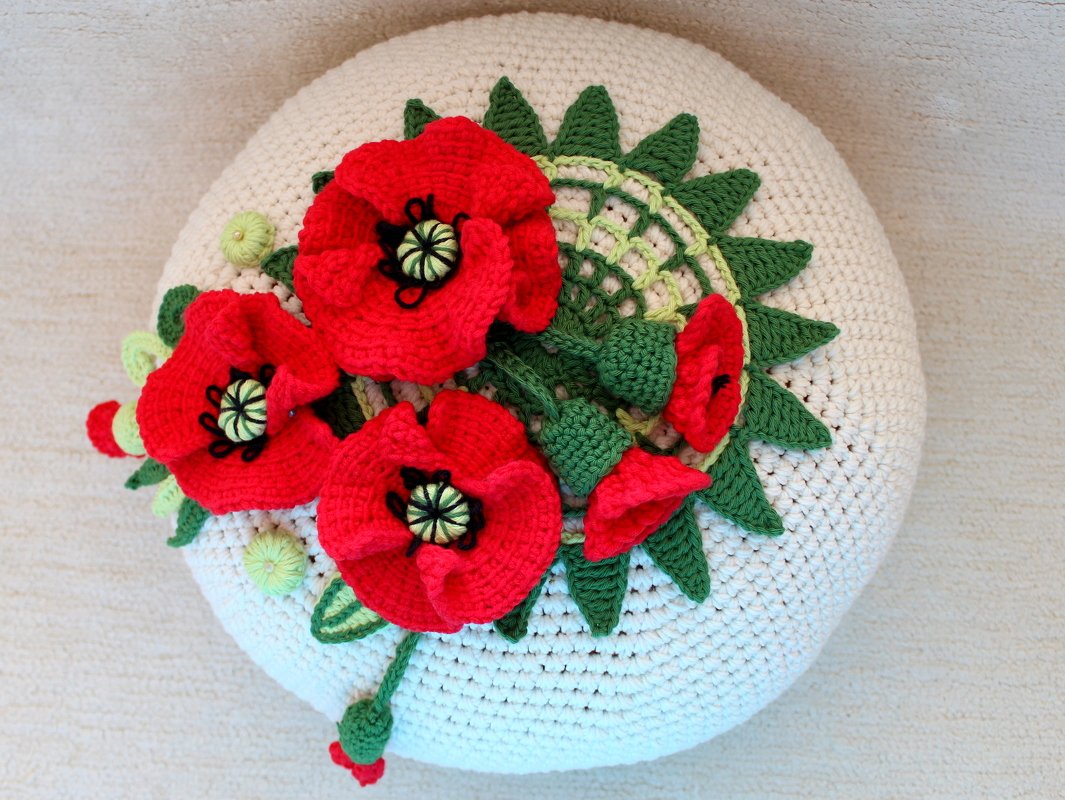 Rundes cremefarbenes Häkelkissen mit roten 3D-Mohnblumen und grünen Blättern