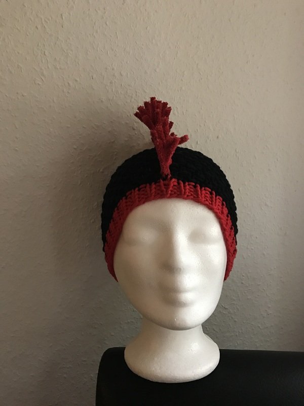 Schwarz-rote Strickmütze mit rotem Zierelement auf Styroporkopf