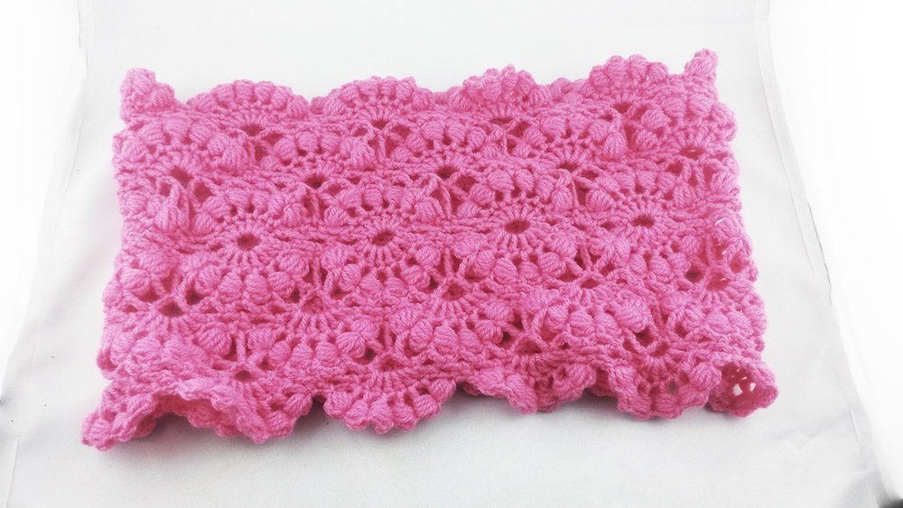 Rosa gehäkelter Loop-Schal mit Muschel- und Noppenmuster auf hellem Hintergrund.