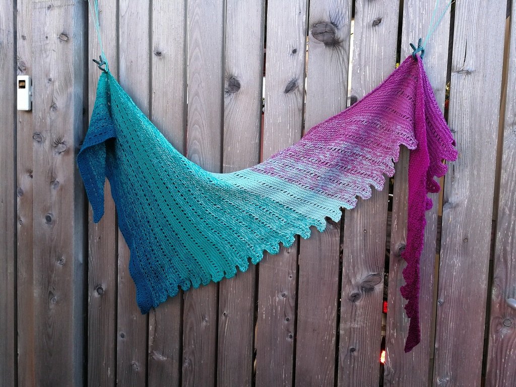Farbintensives gestricktes Tuch mit welligem Rand und Farbverlauf, aufgehängt an einer Holzvertäfelung