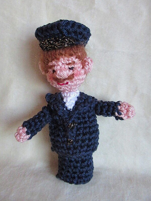 Gehäkelte Amigurumi-Fingerpuppe eines Mannes in dunkler Uniform mit Schirmmütze