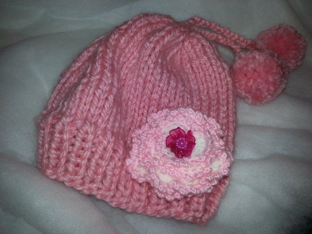 Rosa dick gestrickte Babymütze mit Häkelblüte und zwei Bommeln