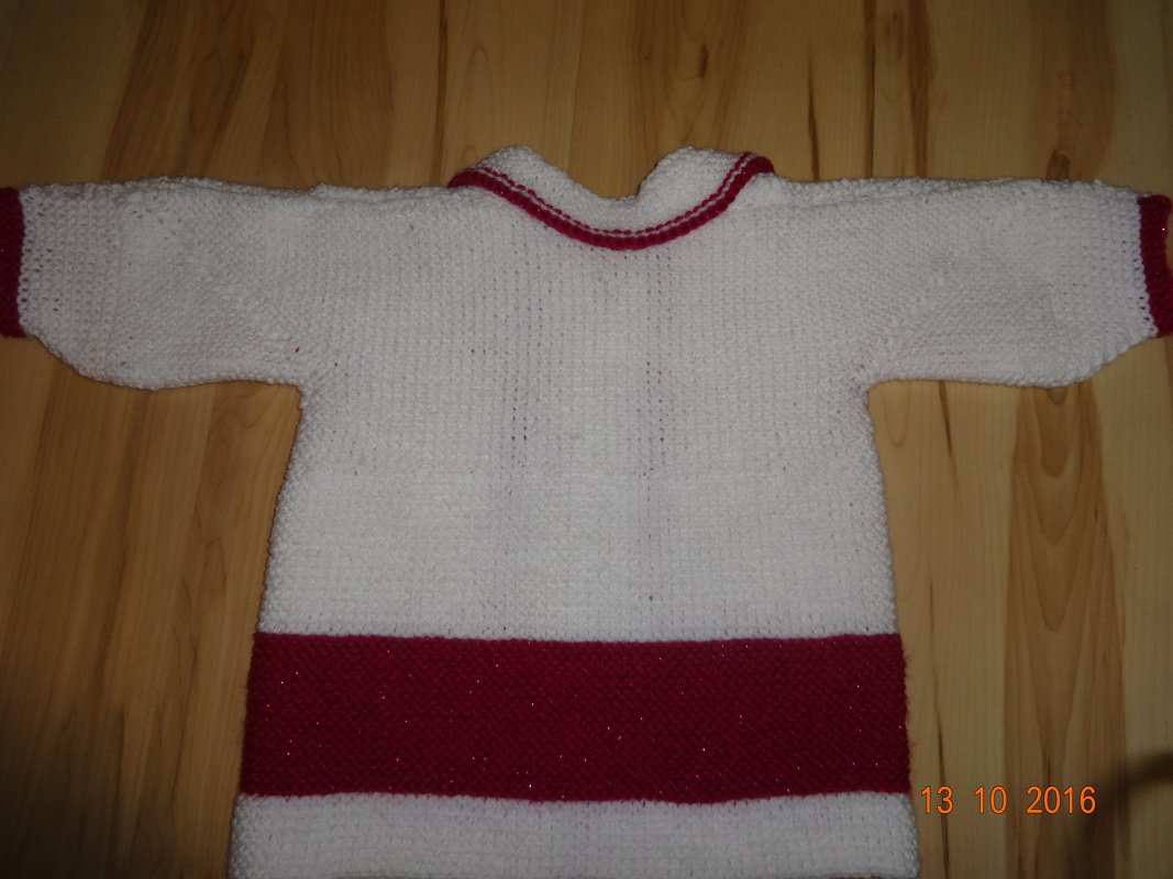 Gestrickte weiße Babyjacke mit breitem roten Saum und roten Bündchen, flach auf Holz