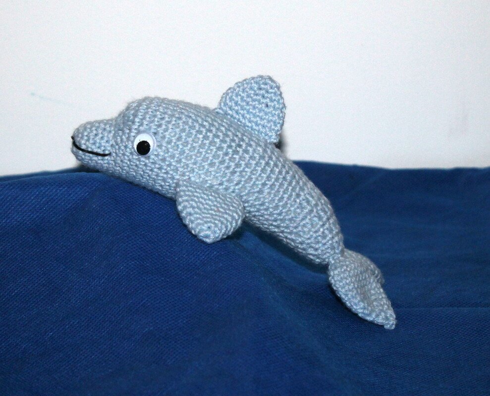 Hellblauer gehäkelter Amigurumi-Delfin mit angenähten Flossen auf dunkelblauem Stoff