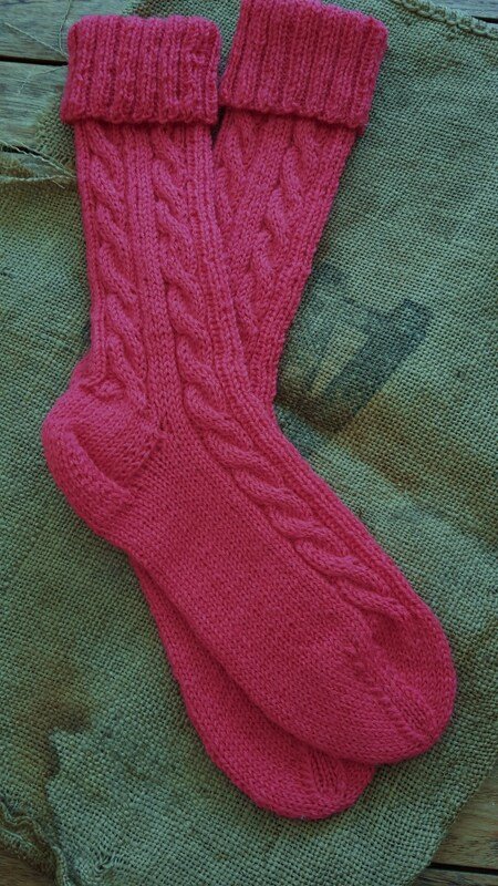 Gestrickte fuchsiafarbene Damensocken mit Zopfmuster auf grünem Stoff