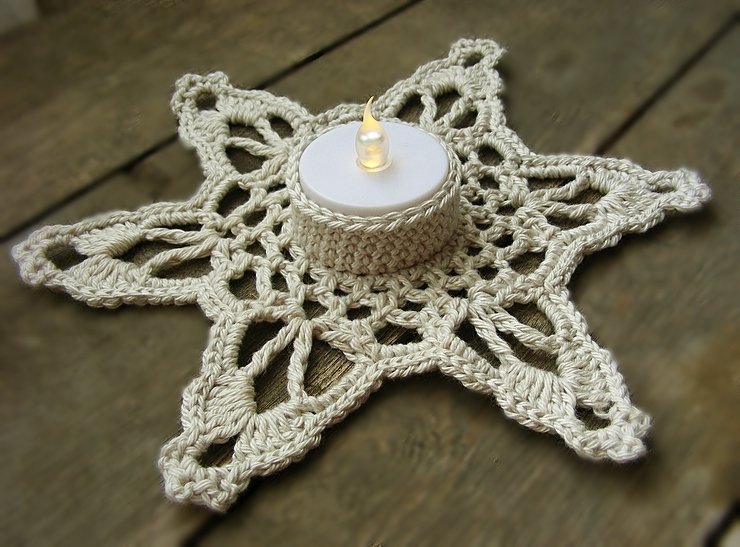 Cream crocheted star mat with a lit LED tea light in a central holder on a wooden surface