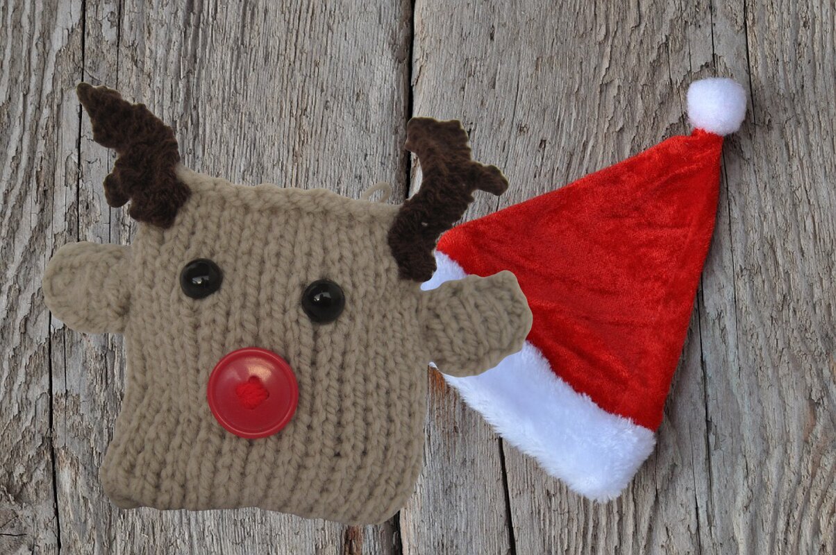Gestrickter Rentierkopf mit Geweih und roter Knopfnase auf Holzhintergrund.