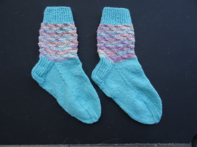 Paar gestrickter Damensocken in Türkis mit mehrfarbigem, strukturiertem Schaft auf dunklem Hintergrund