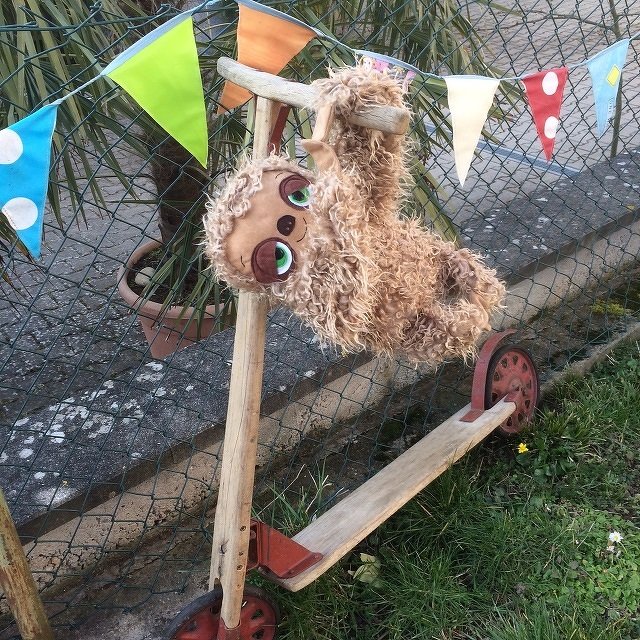 Plüschfaultier mit langem Fell und großen Augen hängt an der Lenkstange eines Holzrollers