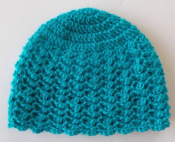 Türkis gehäkelte Babymütze mit Muschelmuster auf hellem Hintergrund