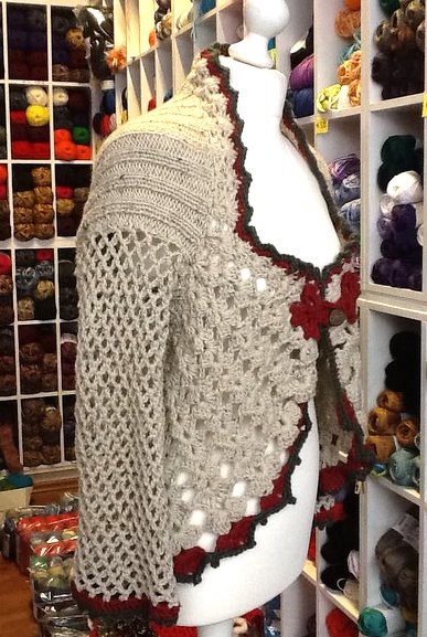 Hellbeige Damen-Strickjacke mit Lochmuster und roten Zierkanten auf einer Schneiderpuppe