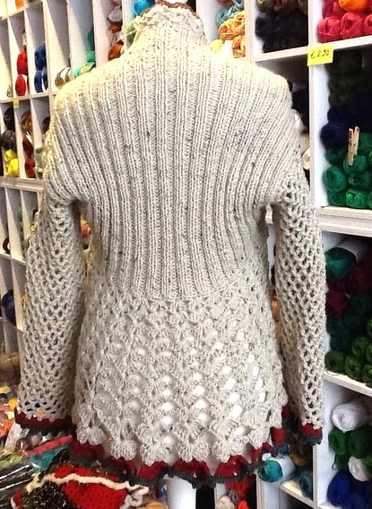 Cremefarbene Strickjacke von hinten mit vertikal geripptem Rückenteil, offenem Lochmuster am Saum und netzartigen Ärmeln