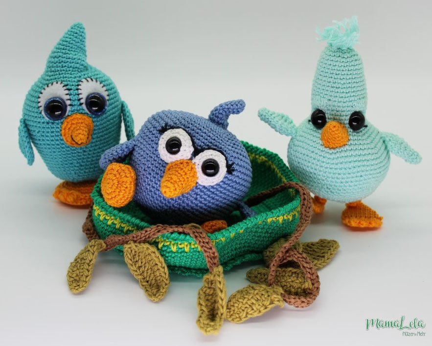 Drei gehäkelte Amigurumi-Vögel in Blau- und Türkistönen, einer sitzt im grünen Nest