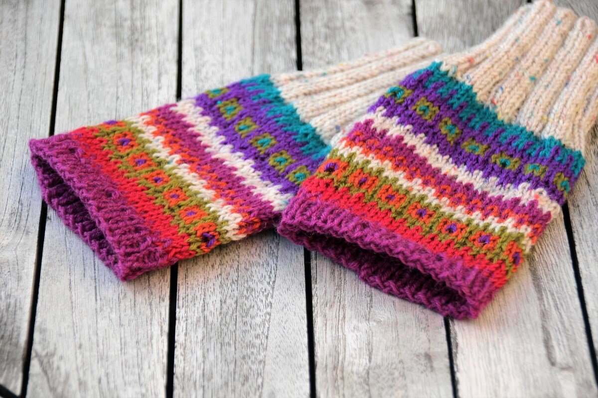 Gestrickte Armstulpen mit buntem Fair-Isle-Muster und beigem Schaft auf heller Holzoberfläche
