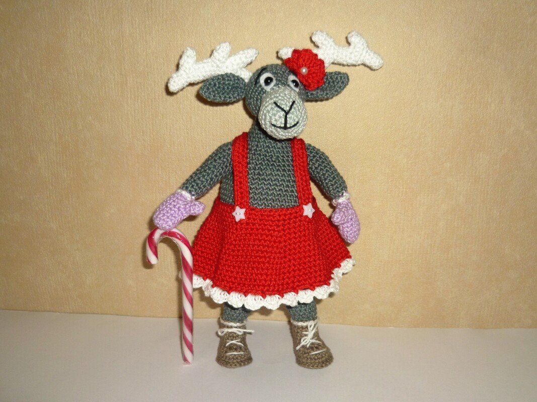 Gehäkeltes Rentier-Amigurumi mit weißem Geweih, rotem Kleid, lila Fäustlingen und Zuckerstange