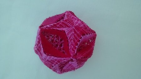 Nahaufnahme eines zusammengenähten, kugelförmigen Stoffanhängers in Rosa und Rot