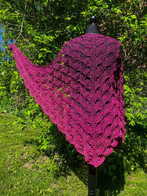 Magenta crocheted triangle shawl with wave openwork on a black mannequin outdoors.