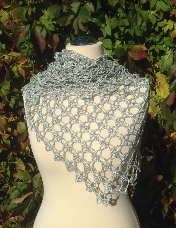 Light grey crocheted lace shawl draped on a mannequin with leafy background.
