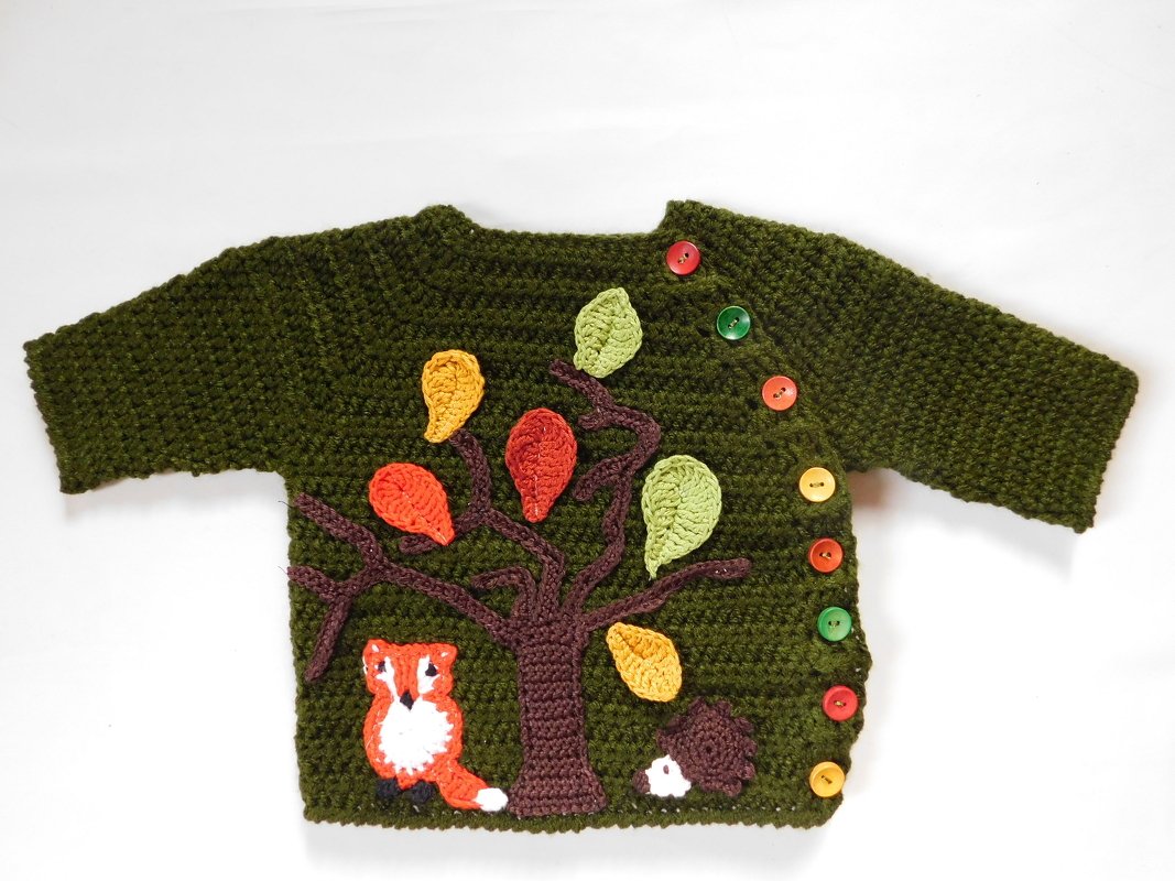 Dunkelgrüne, handgehäkelte Babyjacke mit applizierten Baum-, Blatt- und Waldtiermotiven; seitliche bunte Knopfleiste.