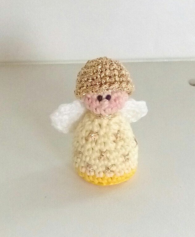 Kleines gehäkeltes Engel-Amigurumi mit goldener Mütze, cremefarbenem Kleid und weißen Flügeln