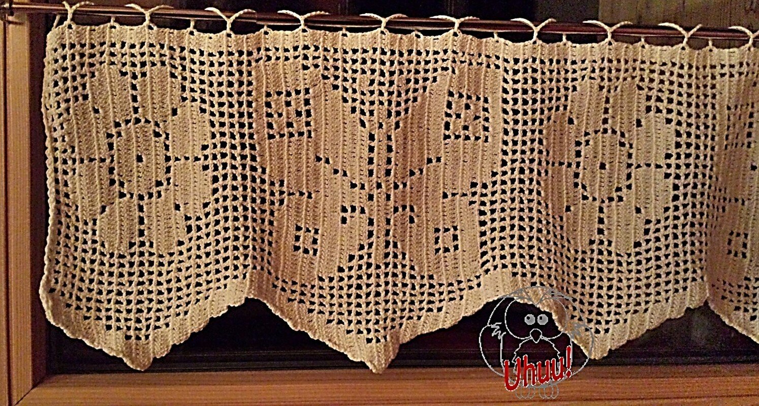 Handgehäkelter cremefarbener Fenstervorhang im Filethäkelstil mit Blattmotiven an einer Holzstange.