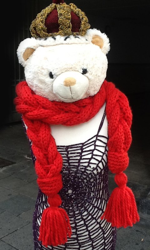 Schaufensterbüste mit Teddykopf trägt dicken, geflochtenen roten Strickschal mit Quasten