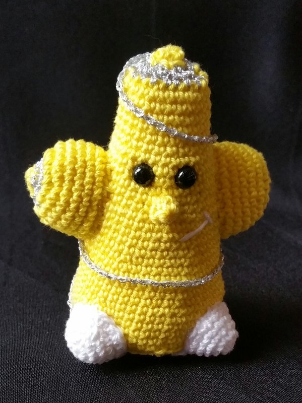 Gelbes gehäkeltes Stern-Amigurumi mit schwarzen Augen und silbernem Zierfaden vor dunklem Hintergrund